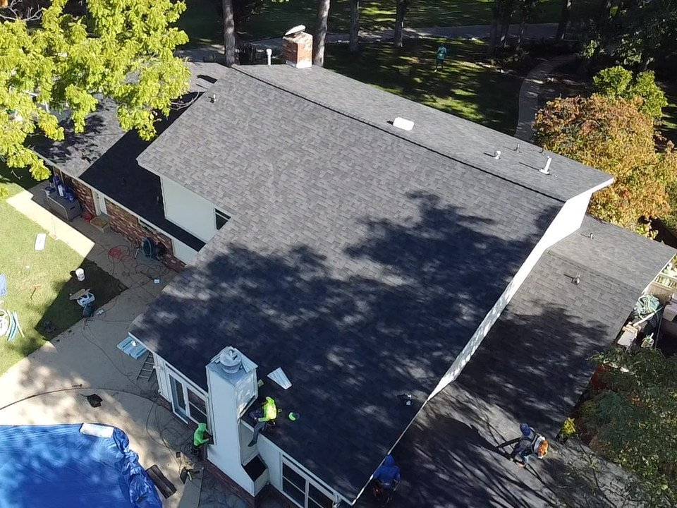 Drone view of a new gray shingle roof on a Bixby home, with the crew finishing the chimney flashing and the pool covered