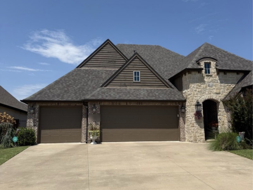 Finished roof replacement with dark shingles on a brick and stone home with a three-car garage in Broken Arrow