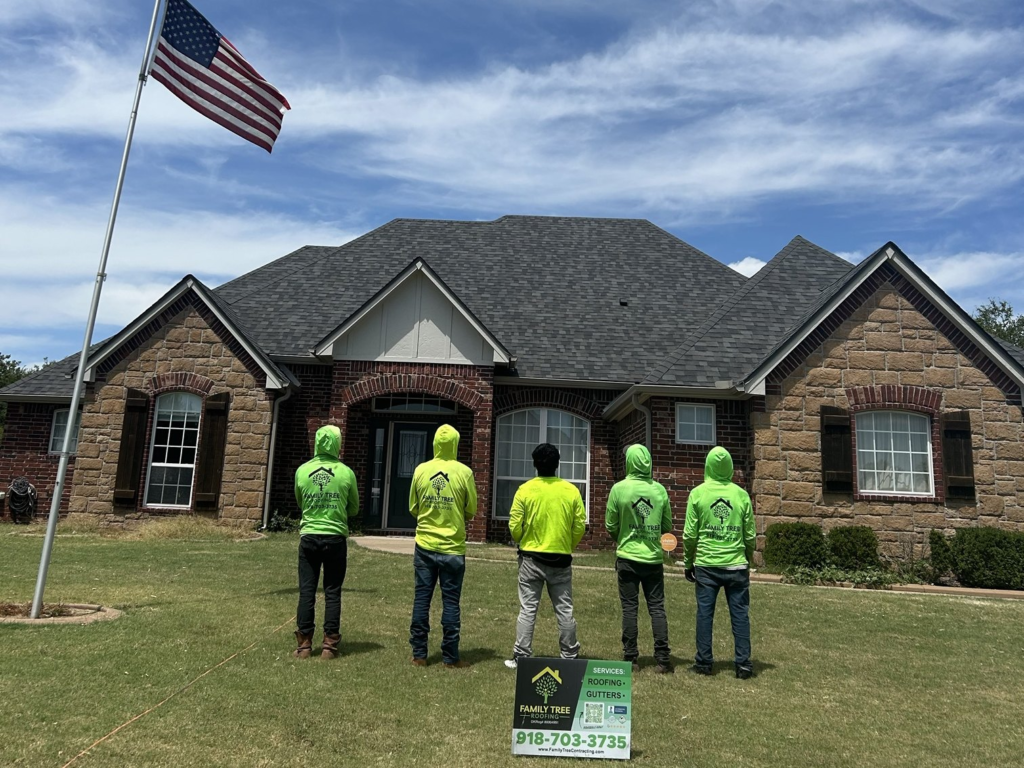 Family Tree Roofing crew standing in front of a finished roof on a brick and stone home in Claremore, with a company yard sign
