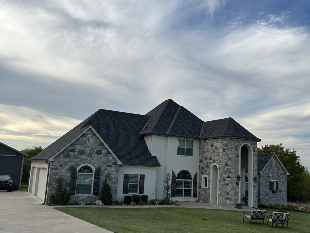 Finished roof replacement with dark shingles on a stone and white brick home in Collinsville