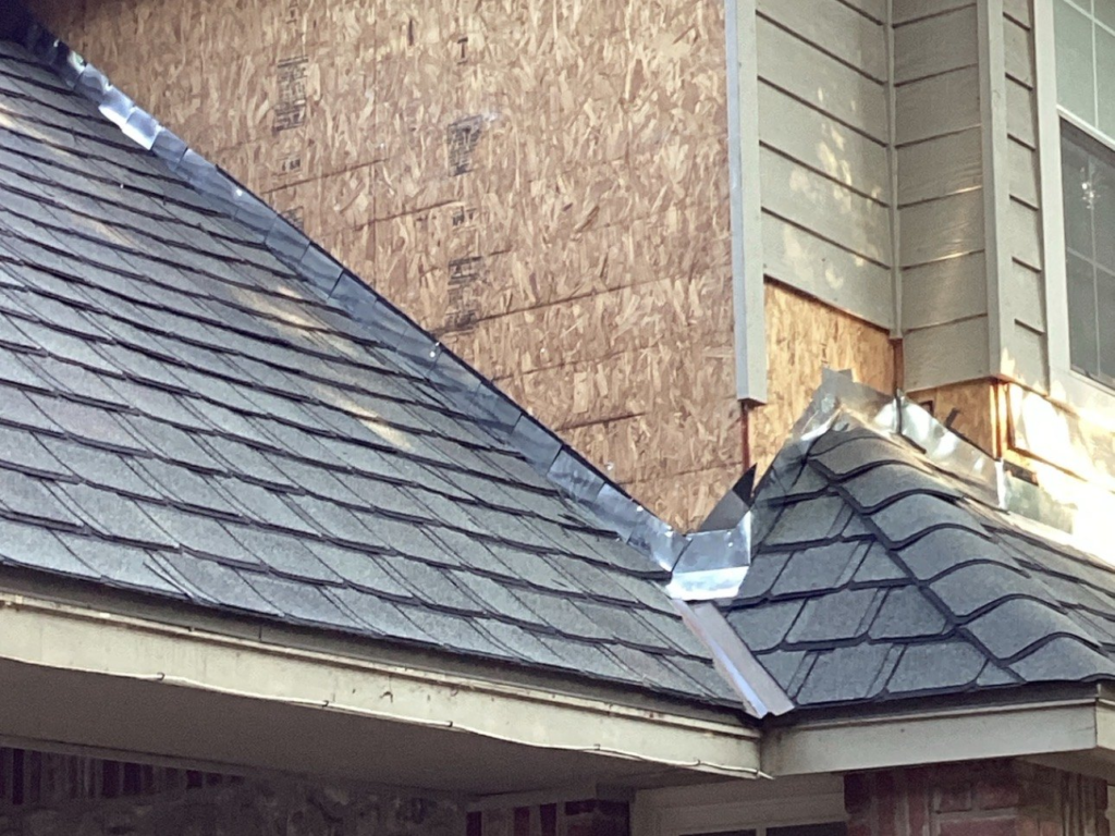 New metal step flashing installed where a shingle roof meets a wall, with the siding removed