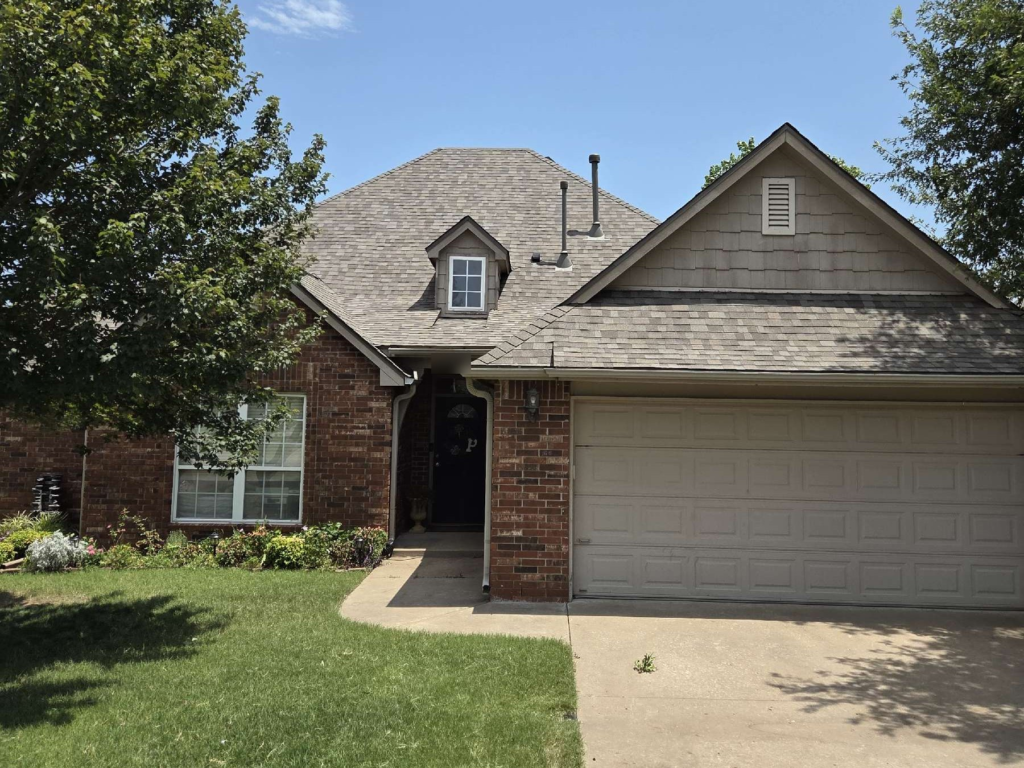 Finished shingle roof with a small dormer on a brick home with a two-car garage in Owasso
