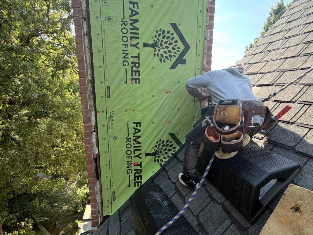Family Tree Roofing installer reflashing a chimney in Bixby, with the chimney wrapped in a vapor barrier before new siding
