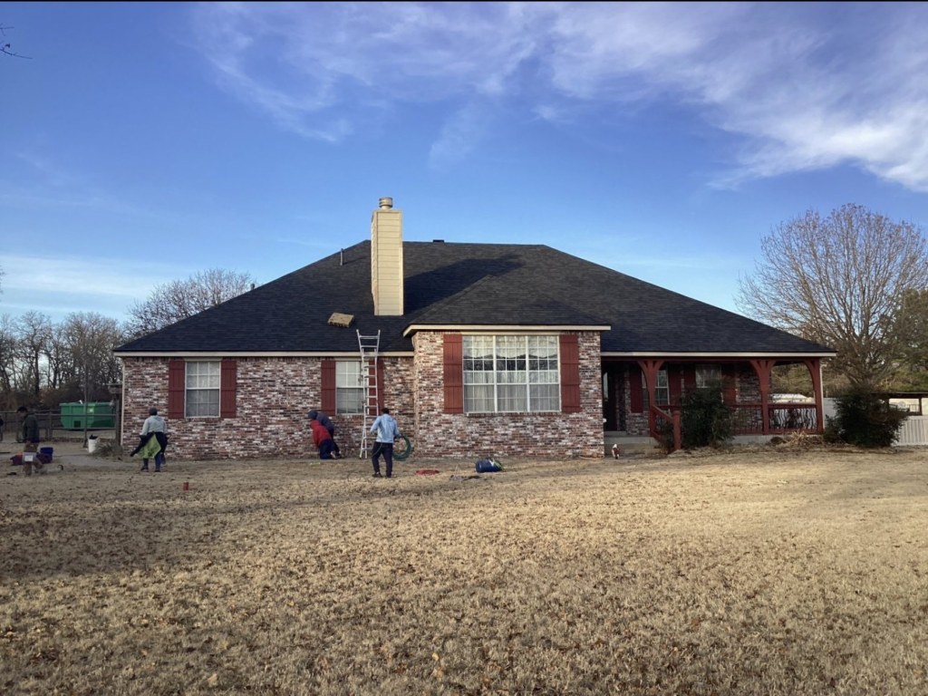 Finished dark shingle roof on a brick ranch home with a covered porch in Sapulpa, with the crew wrapping up in the yard